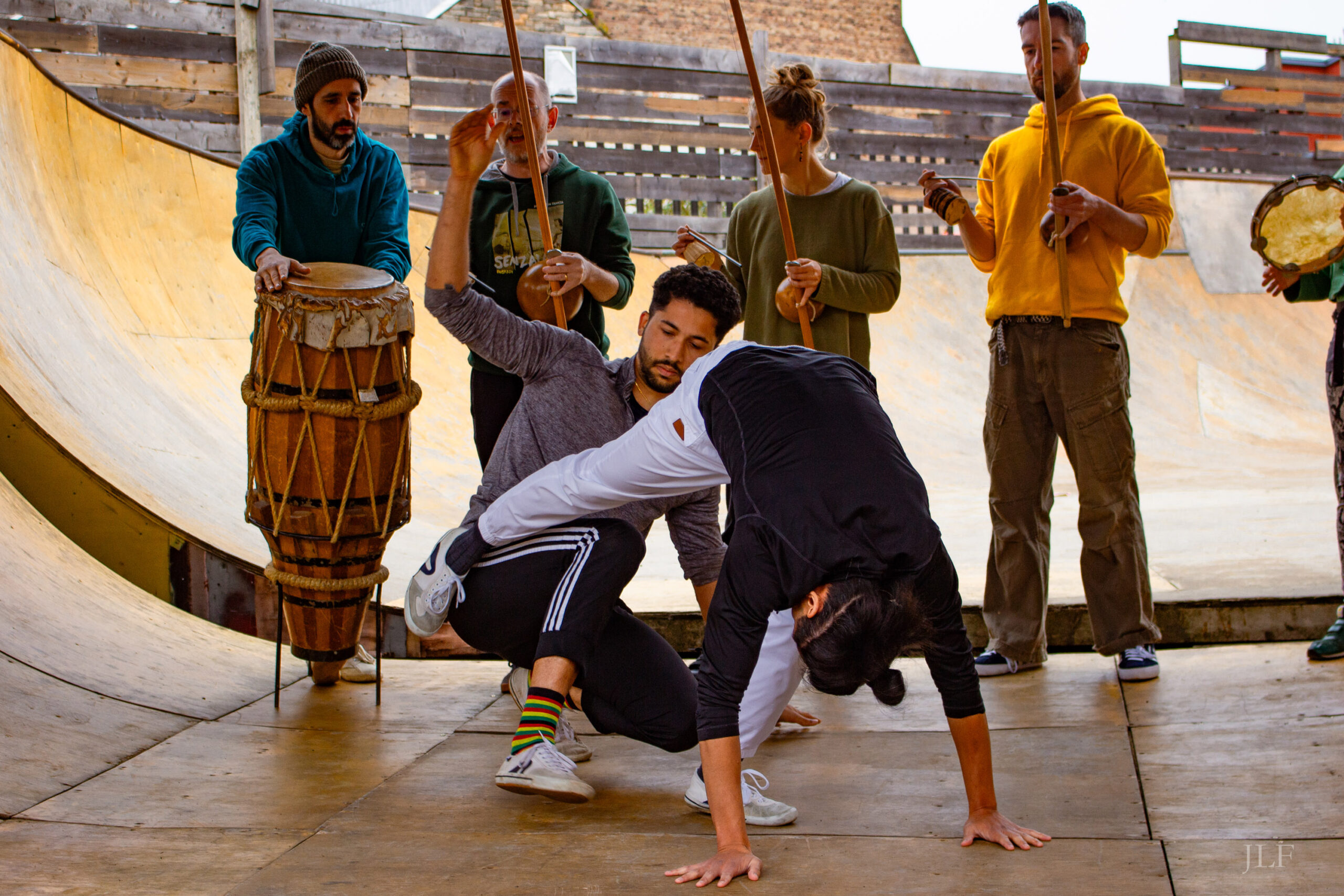 A group of people doing capoeira, 5 persons in a row at the back playing instruments, 2 persons in the foreground dancing.