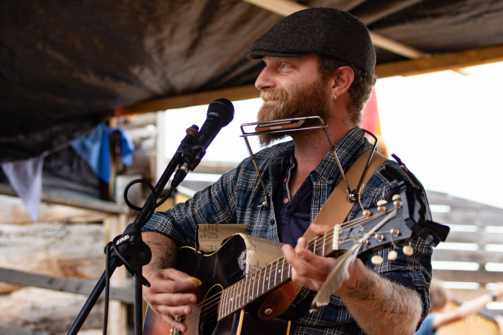 A person playing guitar and harmonica in front of a microphone.