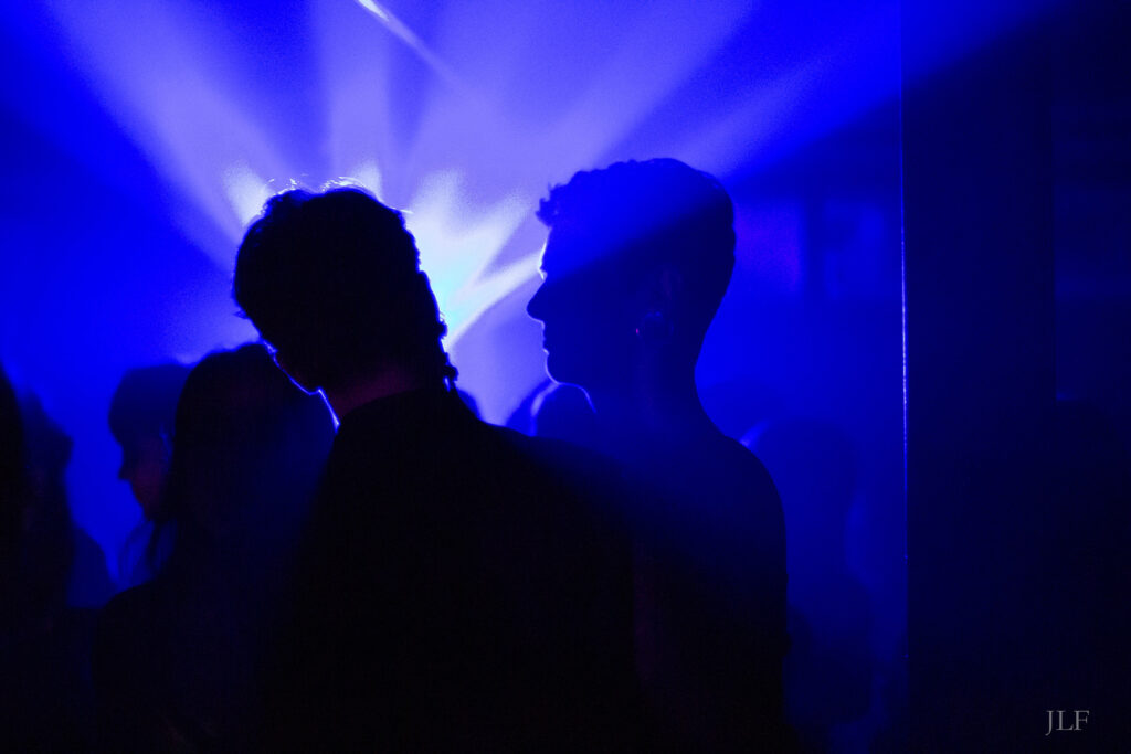 2 people dancing in a night club, bright purple backlight outline the silhouettes.