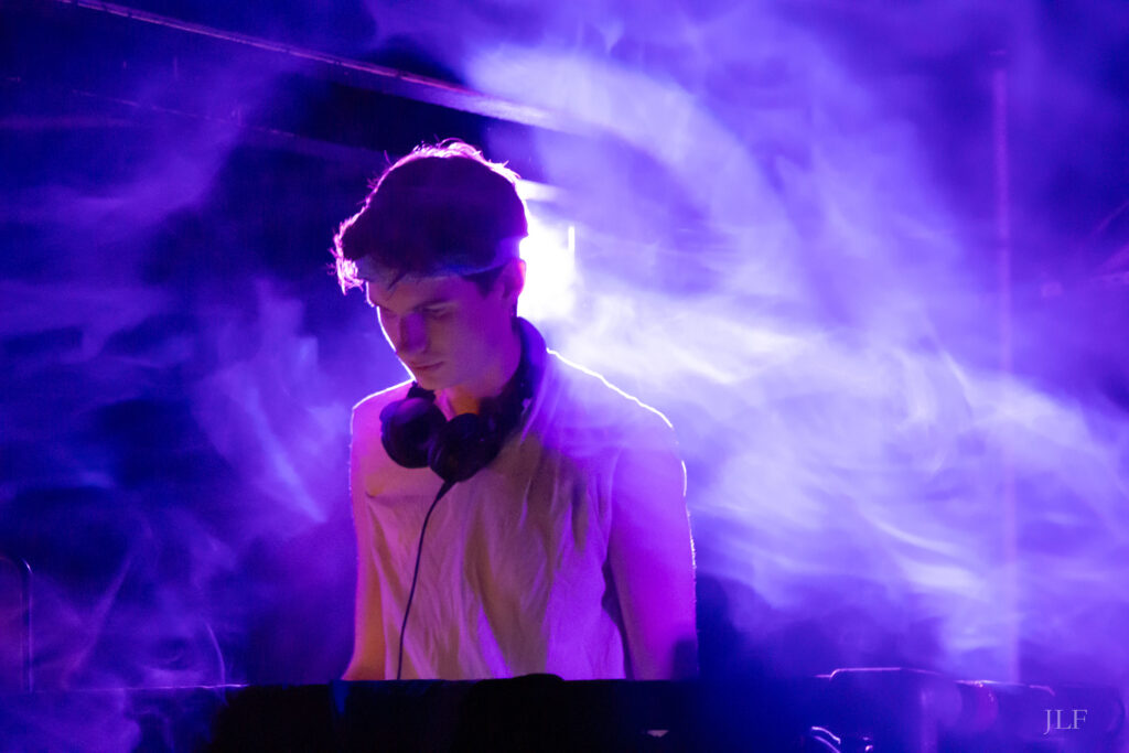 A DJ behind the decks in a night club, purple backlight shining and revealing the silhouette of the subject.